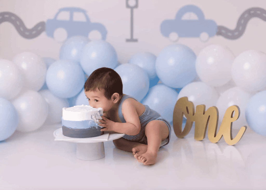 Adorable baby enjoying a blue and white cake during a cake smash photography session in Edmonton, surrounded by blue and white balloons with a gold 'one' sign for a first birthday celebration