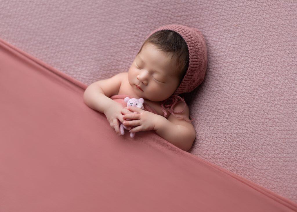 Newborn curled up in womb-like pose, wrapped in a textured knit blanket.
