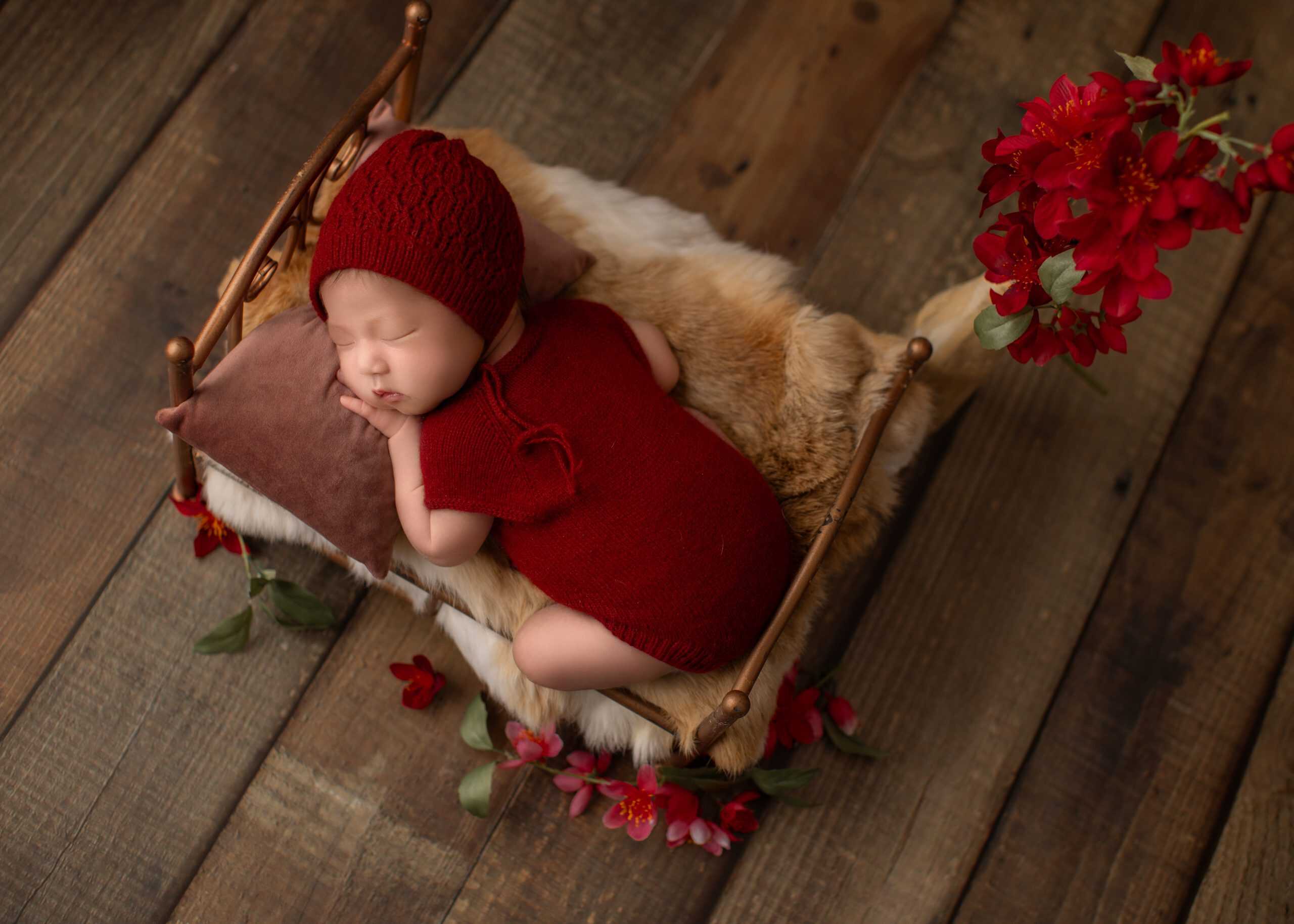 Newborn in a red-toned setup with soft textures and natural styling.