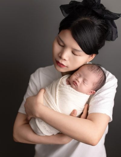 Mom holding newborn close, cheek to cheek, in soft natural light.