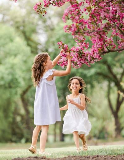 sibling girls running under the flower tree in Edmonotn legislation buiding during family photoshoot