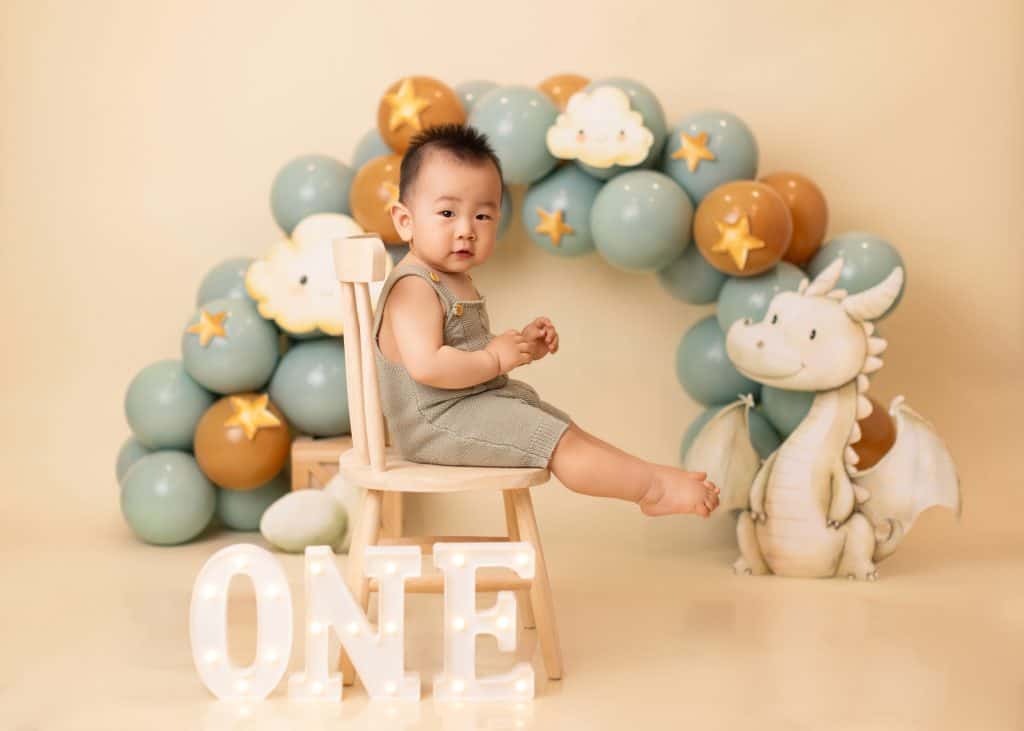 baby sitting on a chair with custmized dragon cake smash theme which is a fully custmized setup created by Little One Photography