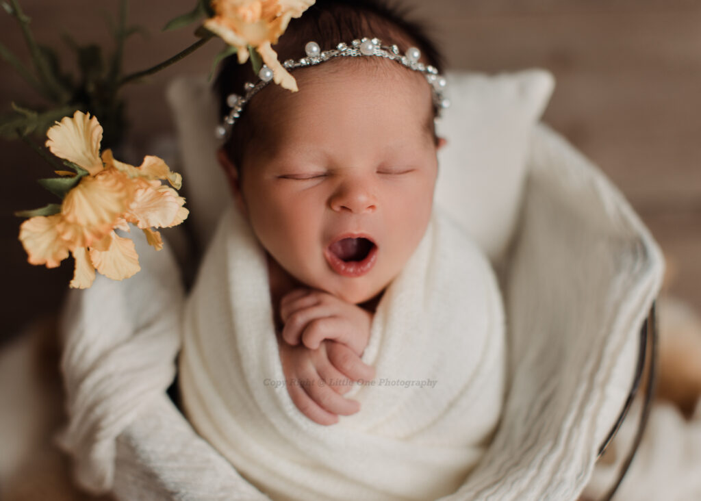 Wrapped newborn baby photographed in a warm, neutral studio setting