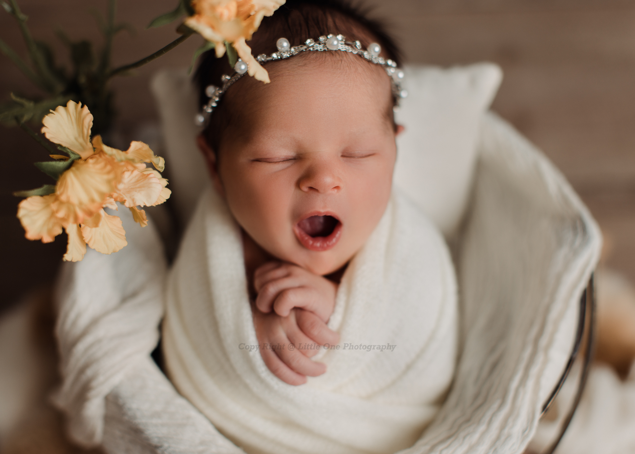 Wrapped newborn baby photographed in a warm, neutral studio setting