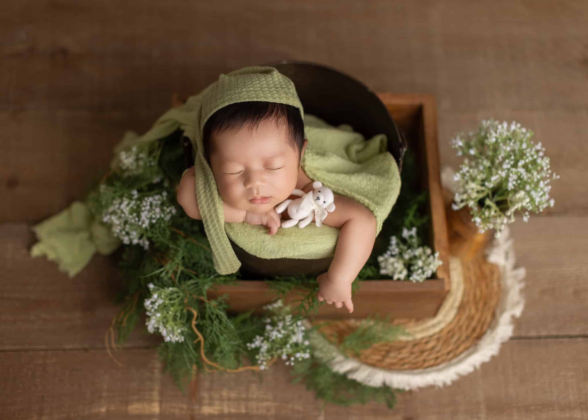 newborn baby wear green lying in a basket with flowers full of spring feeling