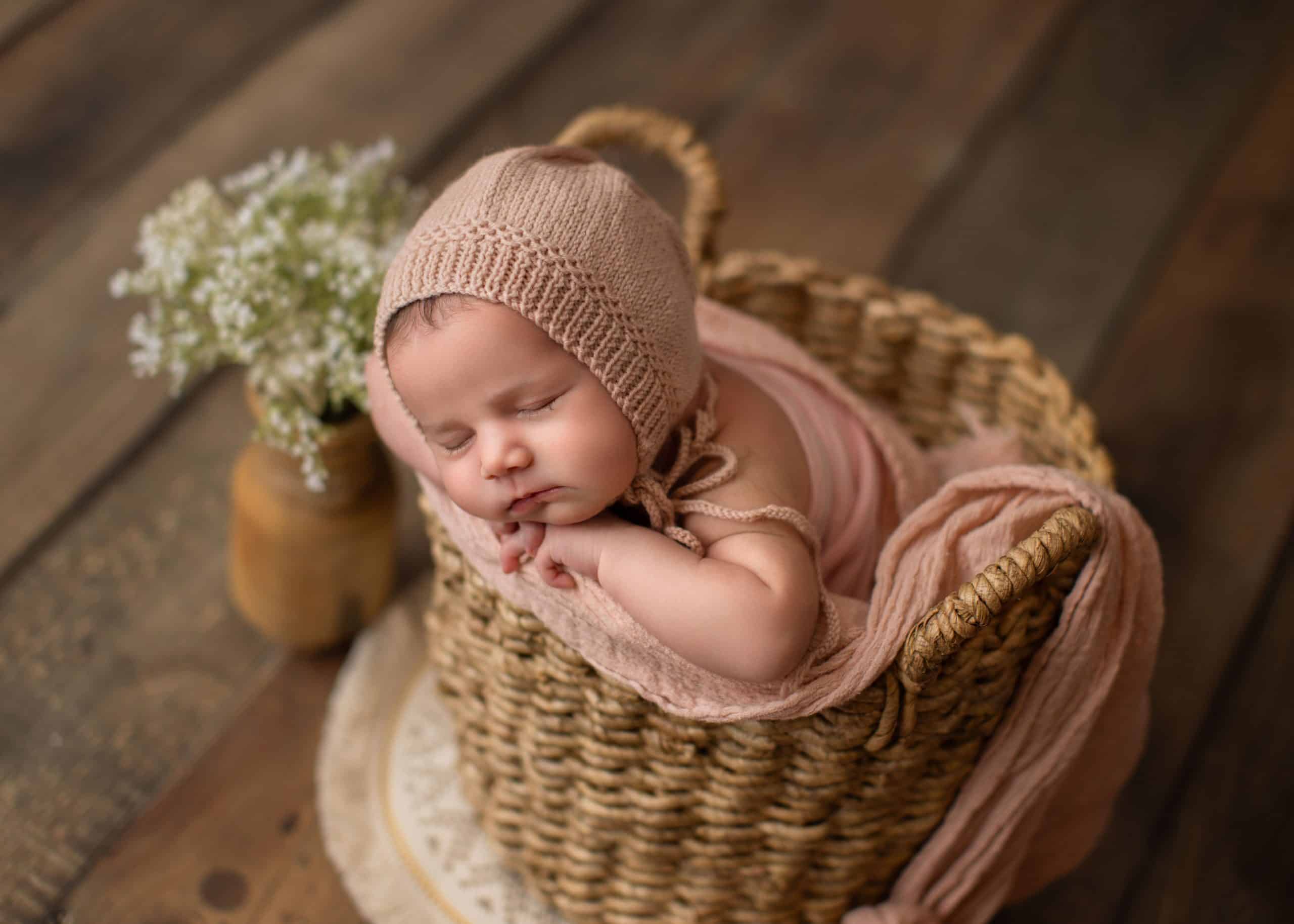 Baby girl sleeping in a cozy basket surrounded by neutral-toned props.