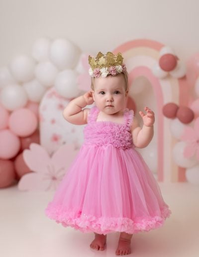 Baby girl during a custom cake smash session with pink decor and birthday cake – photographed in Edmonton studio.