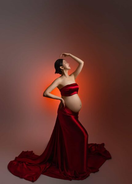A pregnant woman in a red dress posing for an edmonton materenity photo.