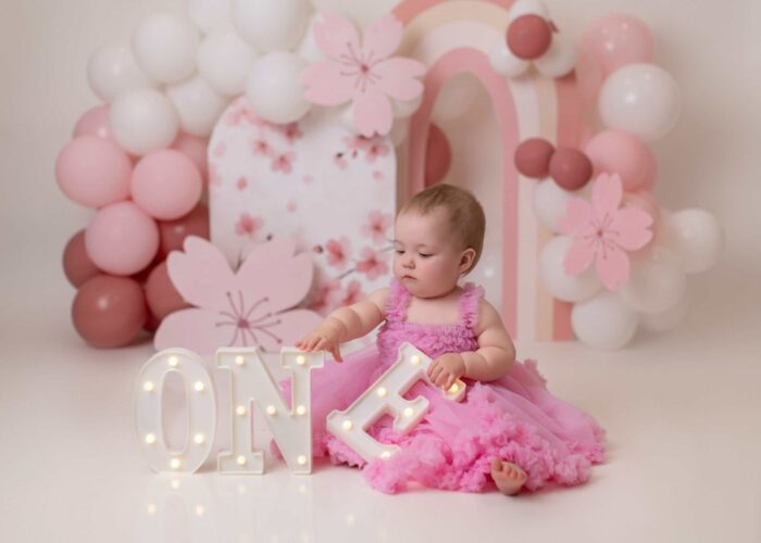 Edmonton cake smash photo featuring pink flowers, white ballons, and a dainty setup for a baby girl’s first birthday.